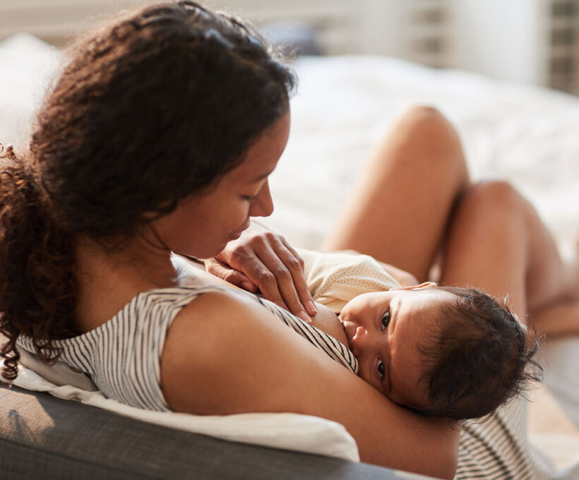 Mulher, jovem e negra, amamentando o bebê com a boca bem posicionada na aréola, uma boa prática do aleitamento materno