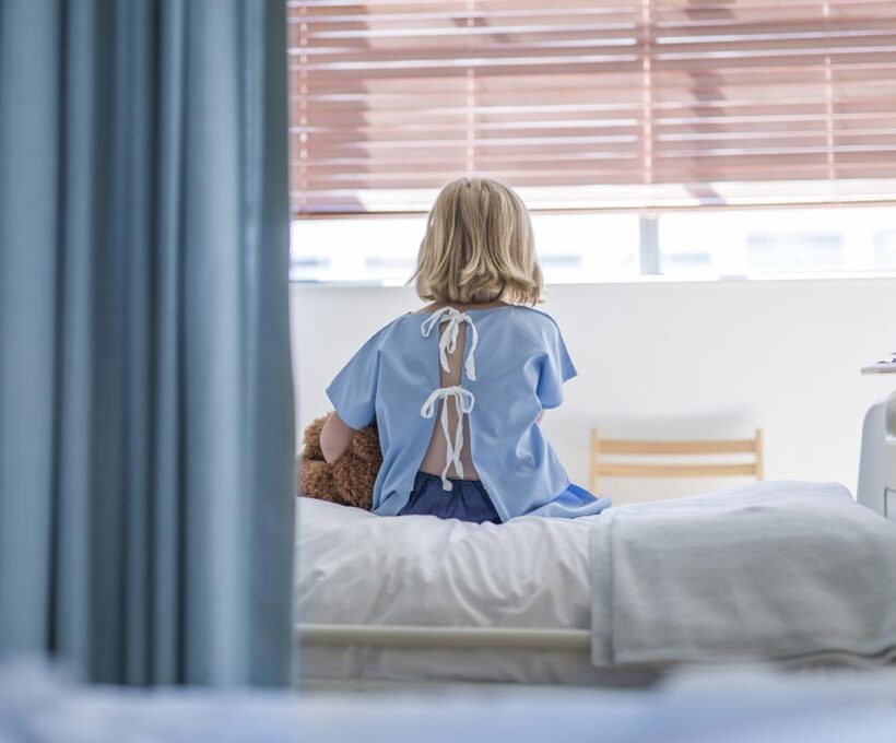 Menina sentada na cama de hospital por causa de possível câncer infantil