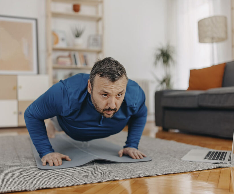 Homem praticando exercício em casa na sala olhando treino online no notebook