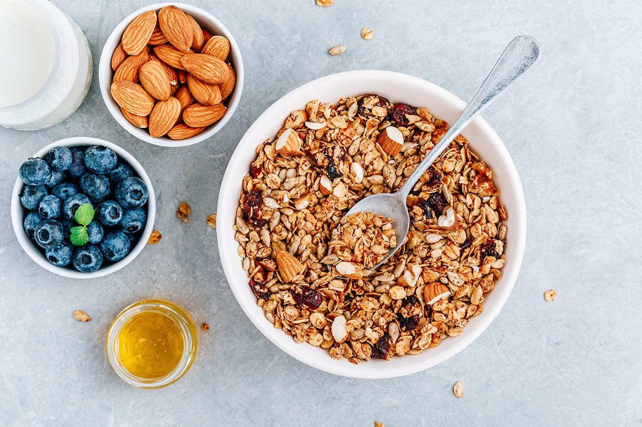 Cereais de granola com mirtilos frescos, amêndoas, leite e mel no café da manhã.